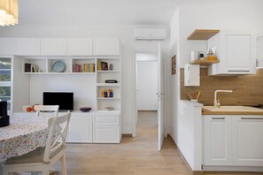 Eine moderne Küche mit weißen Schränken, einer Holz Arbeitsplatte und einem eingebauten Backofen. Es gibt eine Essecke mit Tisch und Stühlen sowie ein Bücherregal voller Bücher.