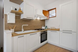 Een moderne keuken met witte kastjes, een houten aanrecht, een gasfornuis, een ingebouwde oven en een raam boven de spoelbak.