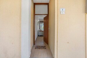 Ein schmaler Flur mit einer Holztür am Ende, einer Fußmatte und einem an der Wand befestigten Schild, das den Standort angibt.