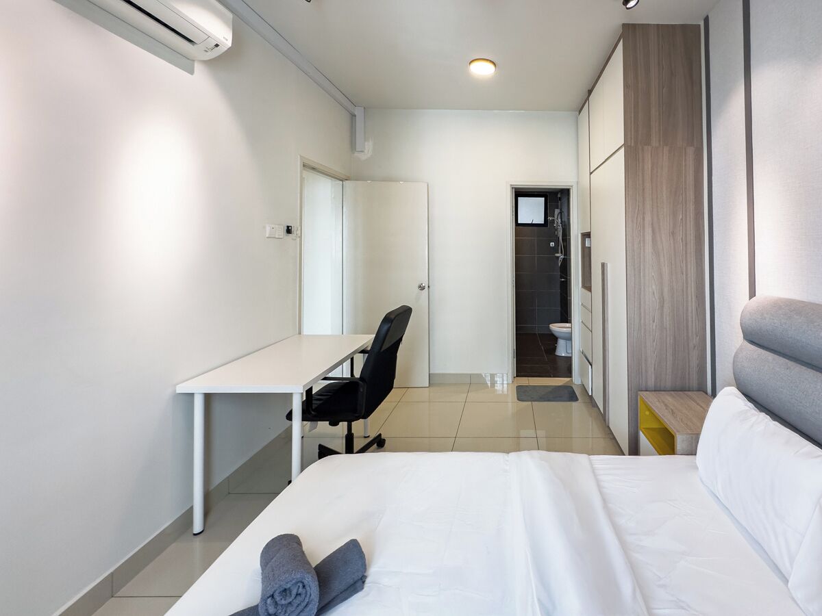 Quarto de hotel moderno com uma cama, uma escrivaninha, uma cadeira e um banheiro visível por uma porta aberta.