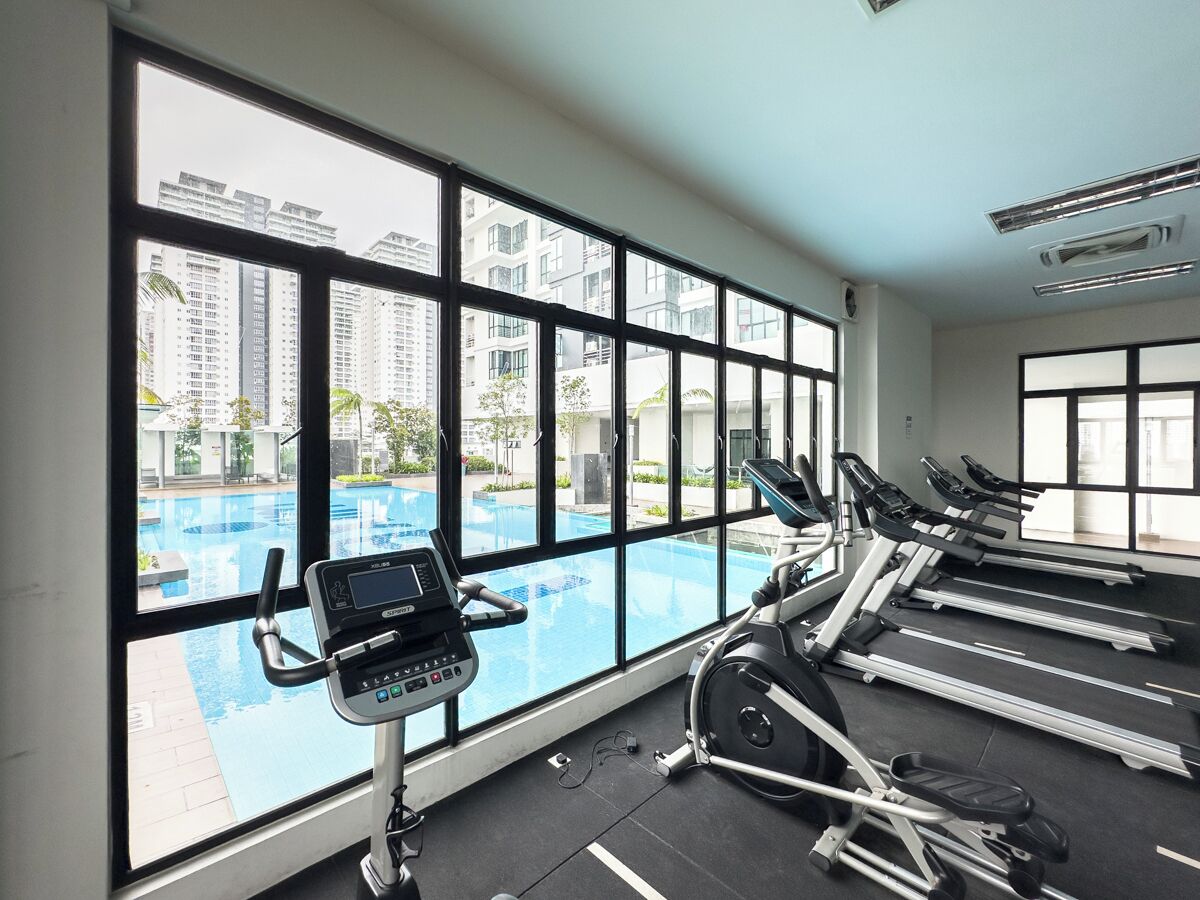 A gym with treadmills, a stationary bike, and a rowing machine, with a large window overlooking a swimming pool and high-rise buildings.