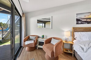 Ein Hotelzimmer mit einem Bett, zwei Sesseln, einem Nachttisch mit Lampe, einem Spiegel und Blick auf eine Terrasse sowie einen Außenbereich.