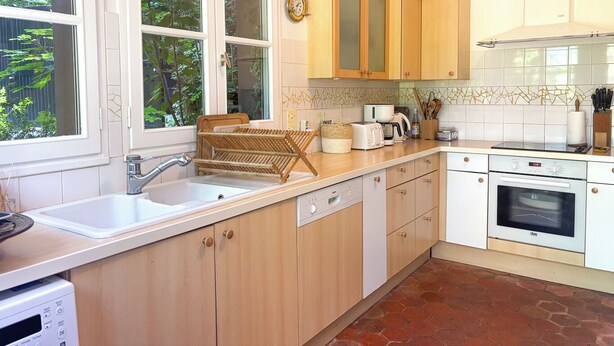 A kitchen with wooden cabinets, a dishwasher, a stove, and a window with a view of greenery. - Pichilemu - Private Beach - Trouville-sur-Mer (Trouville-sur-Mer)
