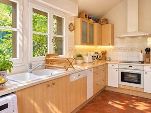 A modern kitchen with wooden cabinets, a built-in oven, and a window with a view of greenery. - Pichilemu - Beach Access - Trouville-sur-Mer (Trouville-sur-Mer)