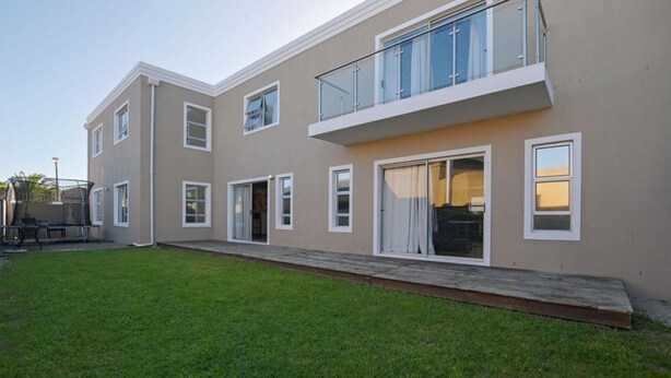 A two-story building with a flat roof, a balcony, and a small grassy yard. - Spacious 5 Bedroom family Home, with a garden and braai facilities (Cape Town)