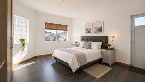A bedroom with a bed, bedside tables, a window with blinds, a chandelier, and framed pictures on the wall. - Spacious 5 Bedroom family Home, with a garden and braai facilities (Cape Town)