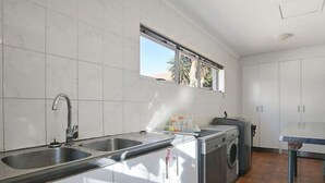 A kitchen with a double sink, a washing machine, and a window above the sink. - Spacious 5 Bedroom family Home, with a garden and braai facilities (Cape Town)