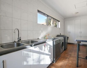 A kitchen with a double sink, a washing machine, and a window above the sink. - Spacious 5 Bedroom family Home, with a garden and braai facilities (Cape Town)