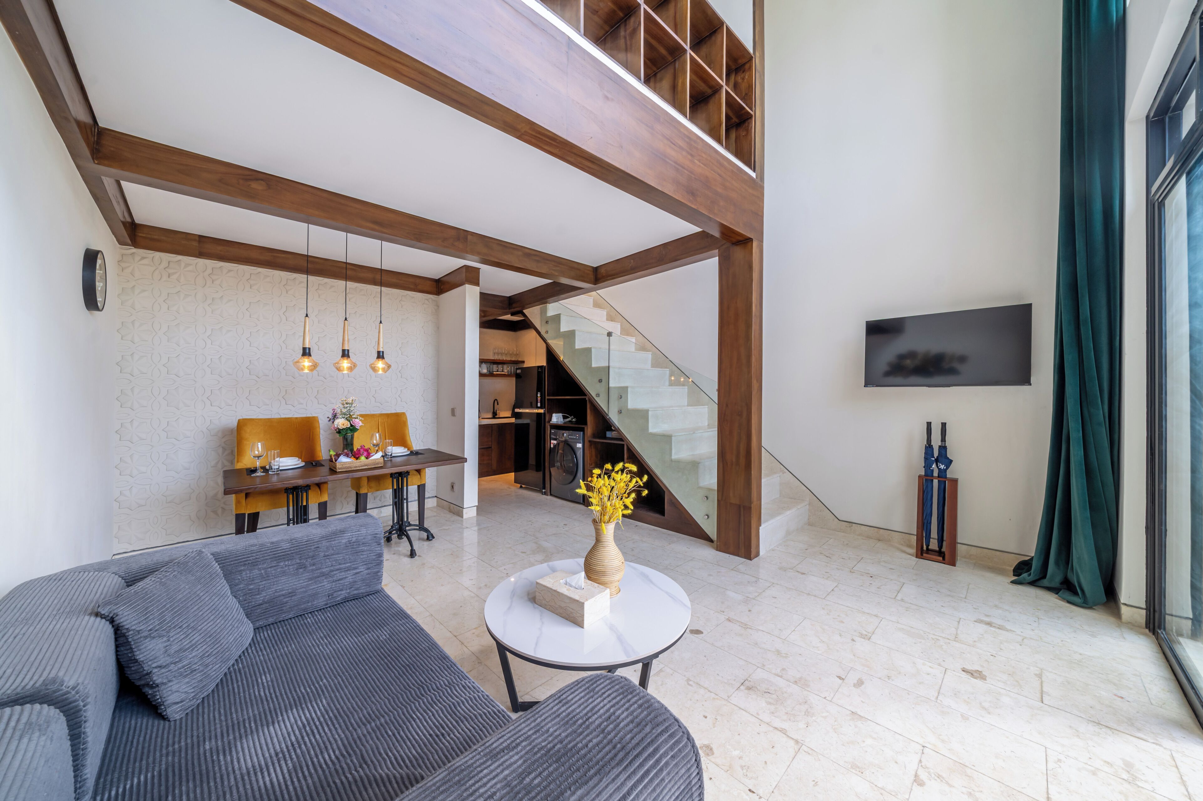 A spacious living area with a sofa, dining table, and a staircase leading to an upper level.