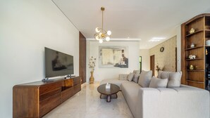 Una sala de estar moderna con un televisor de pantalla plana, un mueble de entretenimiento de madera, un sofá color beige, una mesa de centro y un jarrón decorativo.