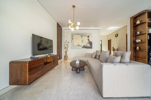 Una sala de estar moderna con un televisor de pantalla plana, un mueble de entretenimiento de madera, un sofá color beige, una mesa de centro y un jarrón decorativo.