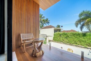 A wooden balcony with a woven chair and a small table, overlooking a lush green landscape and a clear blue sky. - Sunny Villas Ubud (Gianyar)