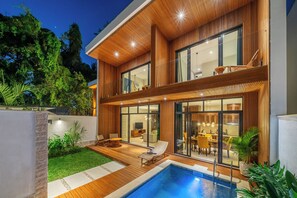 A modern two-story house with a swimming pool, wooden deck, and glass doors leading to a dining area. - Sunny Villas Ubud (Gianyar)