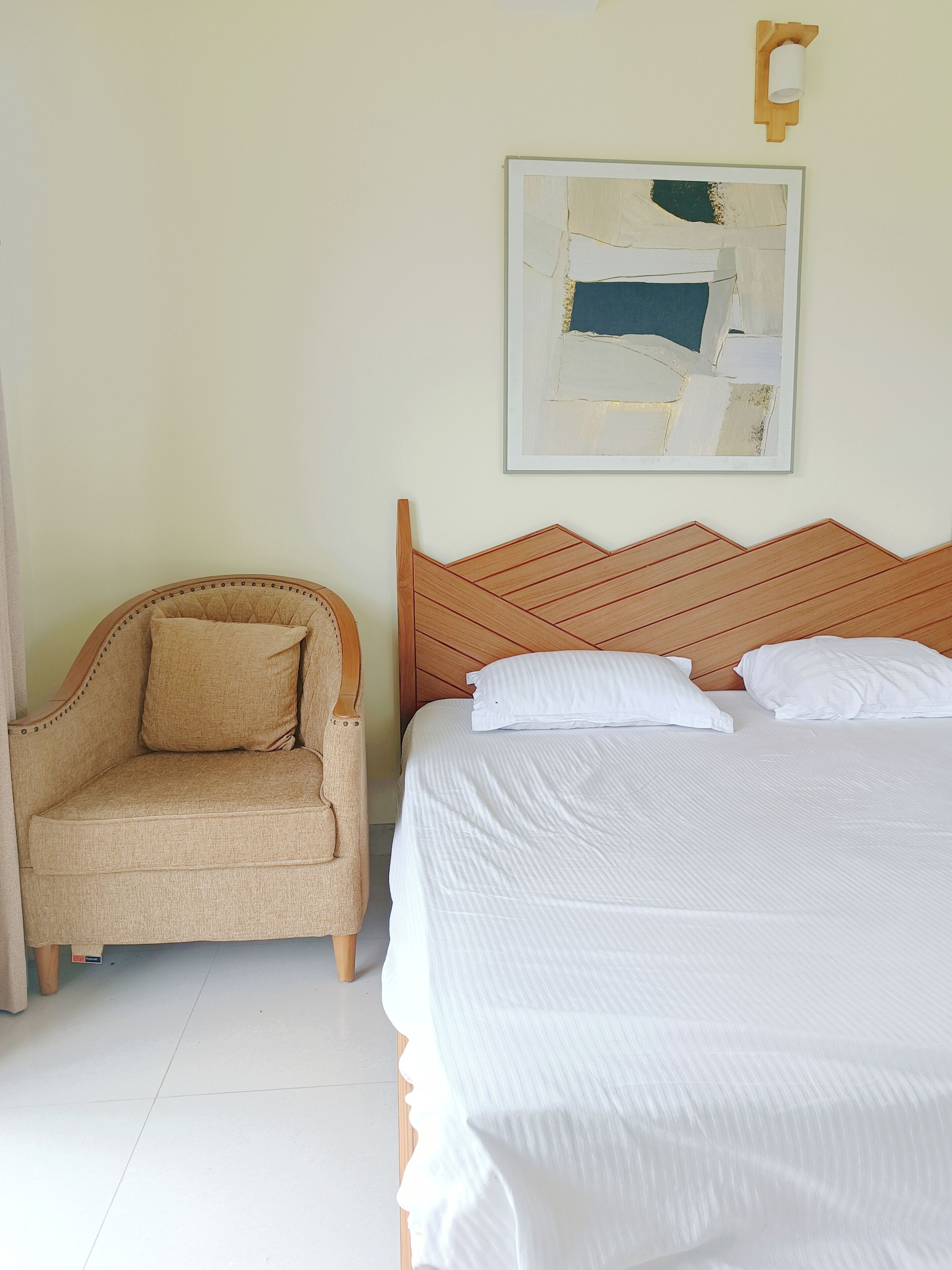 A bedroom with a bed, a chair, and a wall-mounted artwork.