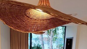 A dining area with a large table, chairs, a woven ceiling light, and a view of a garden through a glass door. - you can enjoy the mountains, rivers greenery & modern luxury resort together. (Rangamati)
