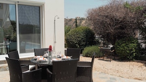 An outdoor dining area with wicker chairs and a table set for two, a grill, and a view of a hillside. - 3BR Panoramic Sea View Villa with Private Pool (Pissouri)