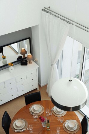 Ein Essbereich mit einem runden Tisch, gedeckt für vier Personen, einer weißen Konsole mit Spiegel, Lampen und einer Vase mit Sonnenblumen.