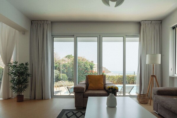 A modern living room with a sofa, a coffee table, a lamp, and a view of a pool and greenery.