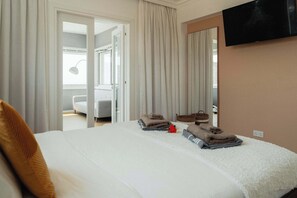 A hotel room with a bed, a television, and a view of a bathroom and a balcony.