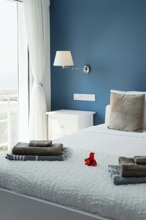 Ein Schlafzimmer mit Bett, Nachttisch, Lampe und Blick durch ein Fenster.