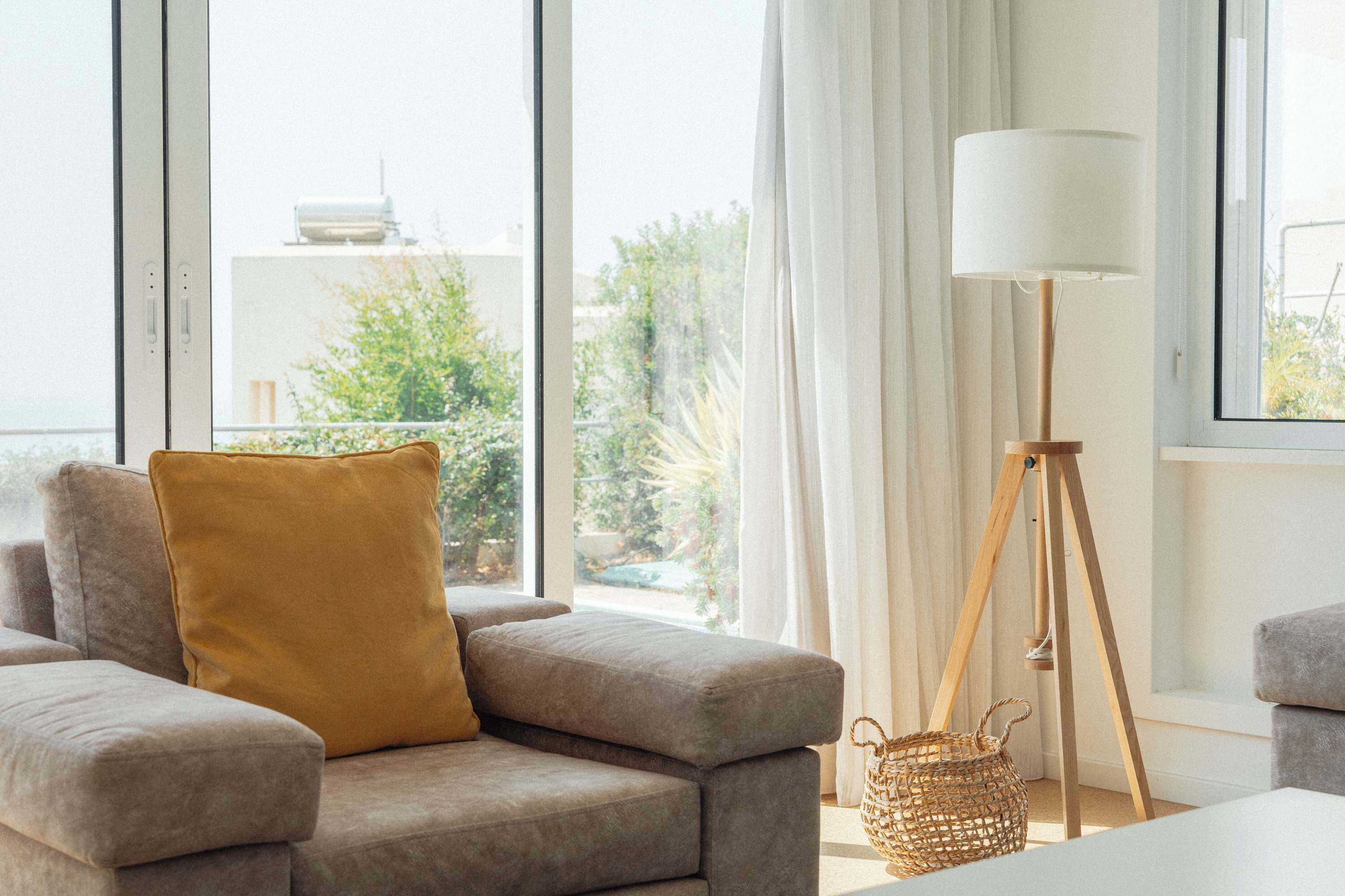 A modern living room with a sofa, a lamp, and a view of greenery outside.