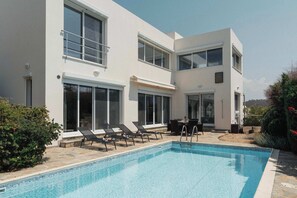 A modern two-story house with a swimming pool, outdoor seating, and a patio area.