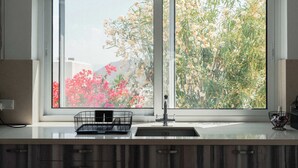 A kitchen with a double sink, a black wire basket, and a window with a view of flowers and greenery. - 3BR Panoramic Sea View Villa with Private Pool (Pissouri)