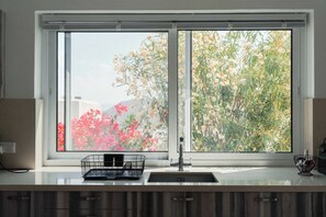 A kitchen with a double sink, a black wire basket, and a window with a view of flowers and greenery.