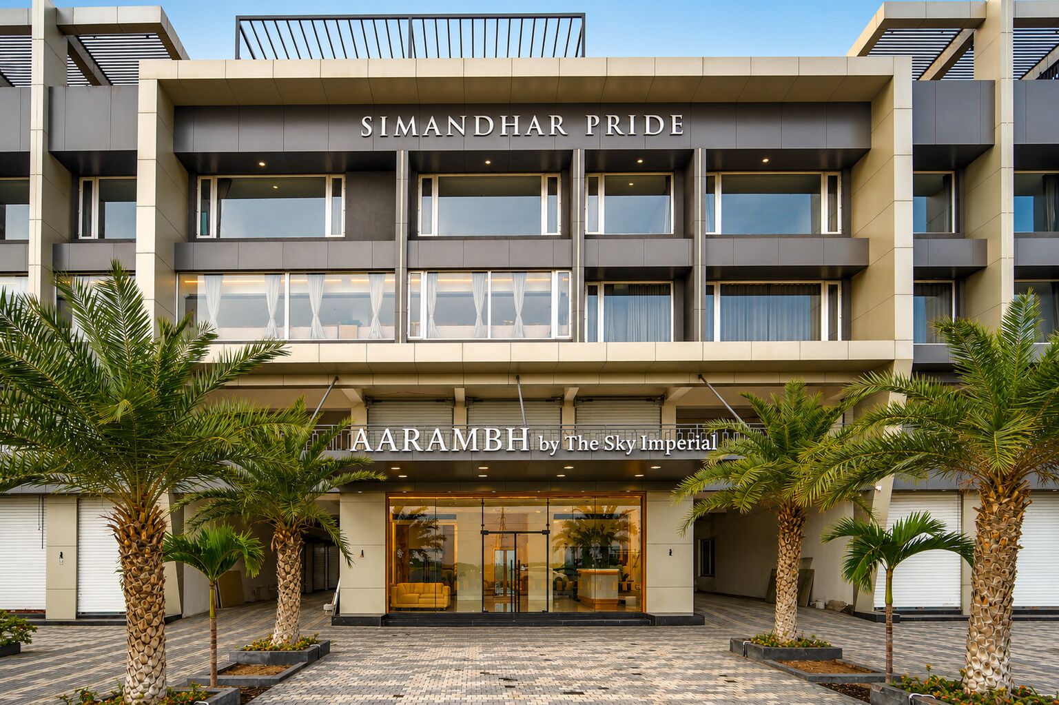 A modern building with 'SIMANDHAR PRIDE' signage, featuring a glass entrance and palm trees in front.
