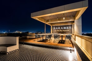 A rooftop dining area with a checkered floor, tables, chairs, and a view of the city at night. - Aarambh by The Sky Imperial Jamnagar (Jamnagar)