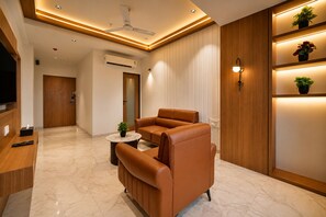 Un salón moderno con un sofá de cuero marrón, una mesita redonda con una planta y un televisor sobre un mueble de madera.