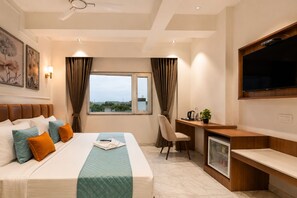 Habitación de hotel con cama, escritorio, silla, televisión y ventana con cortinas.