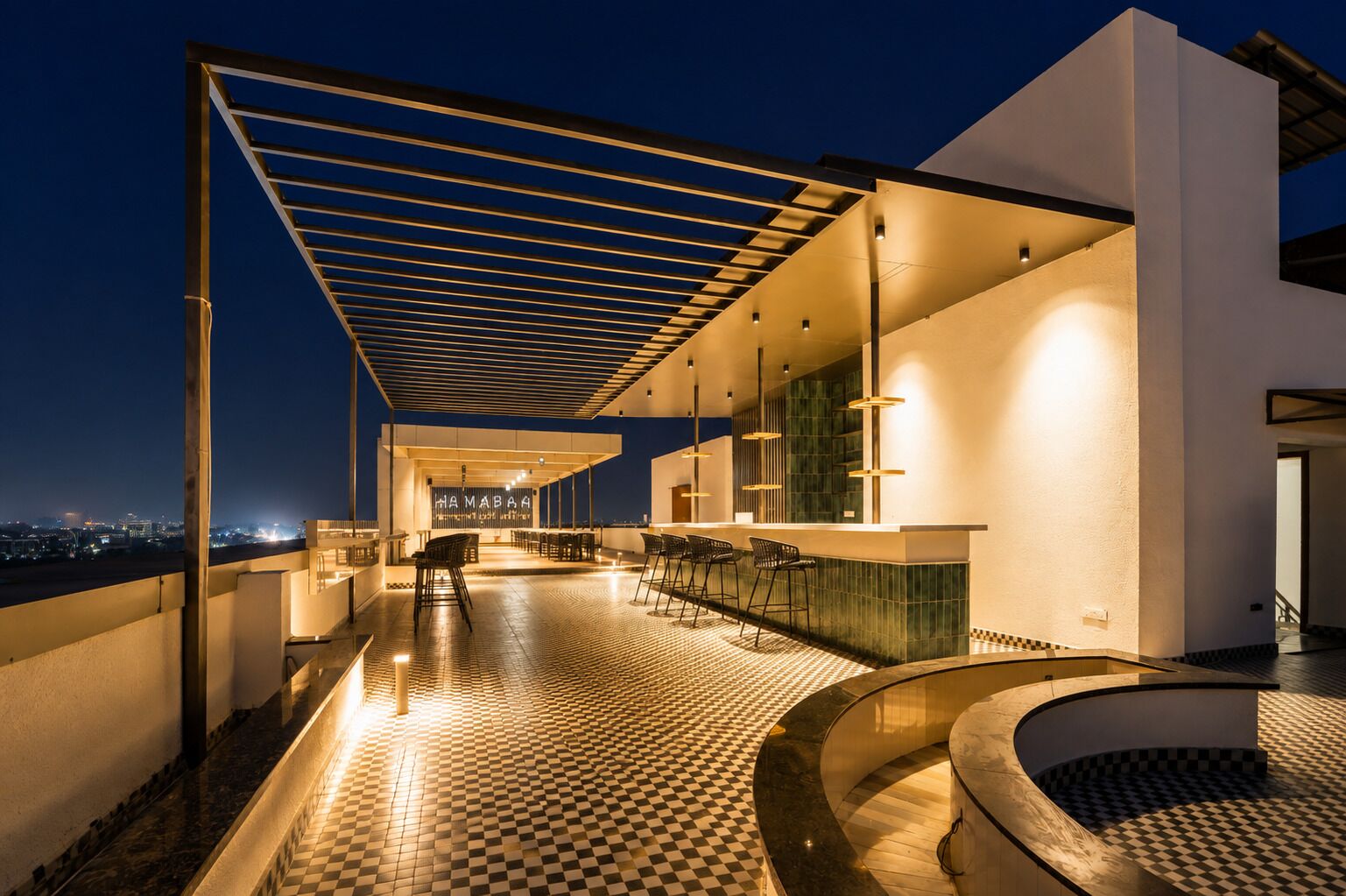 A rooftop bar with a checkered floor, bar stools, and a view of the cityscape at night.