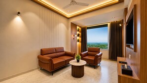 A modern living room with a sofa, armchair, and coffee table, a flat-screen TV, and a large window with a view.