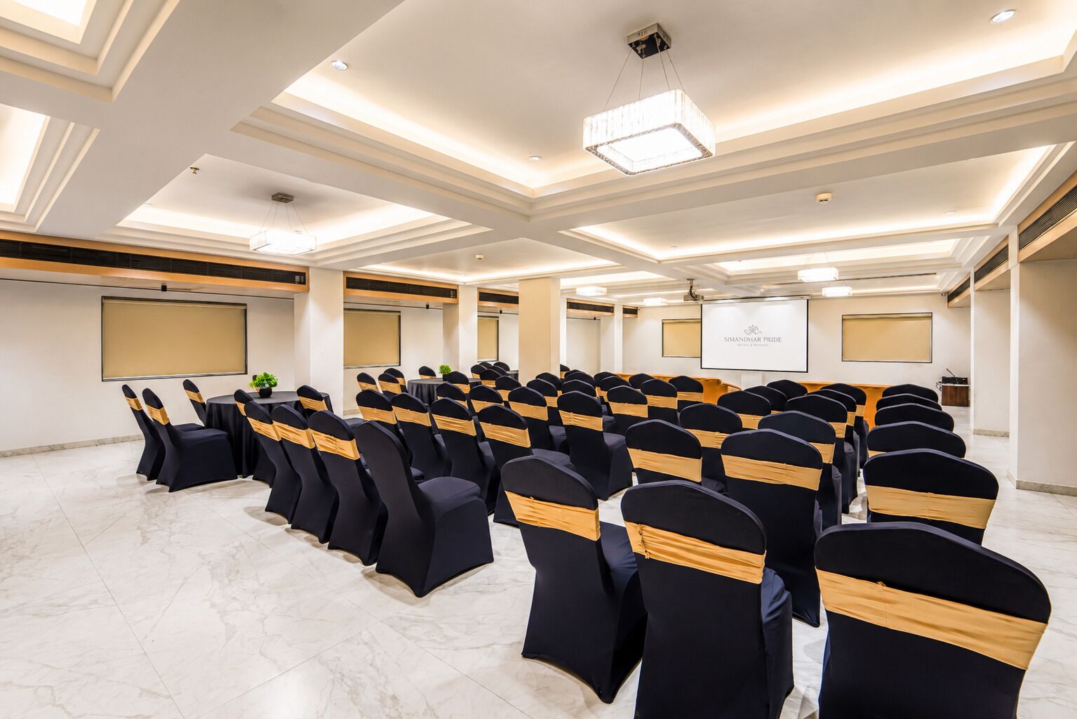 A conference room with rows of chairs, a podium, and a projector screen.
