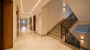 A hotel hallway with a marble floor, a staircase with a metal railing, and recessed lighting.