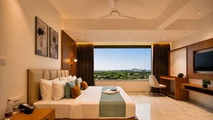 A modern hotel room with a large bed, a desk, a chair, a television, and a view of a cityscape. - Aarambh by The Sky Imperial Jamnagar (Jamnagar)