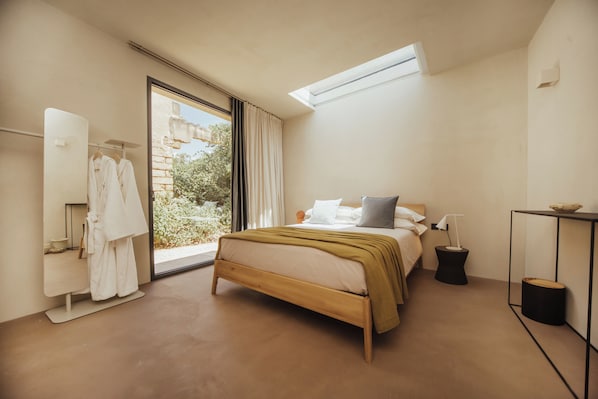 A bedroom with a bed, a bedside table, a mirror, and a window.
