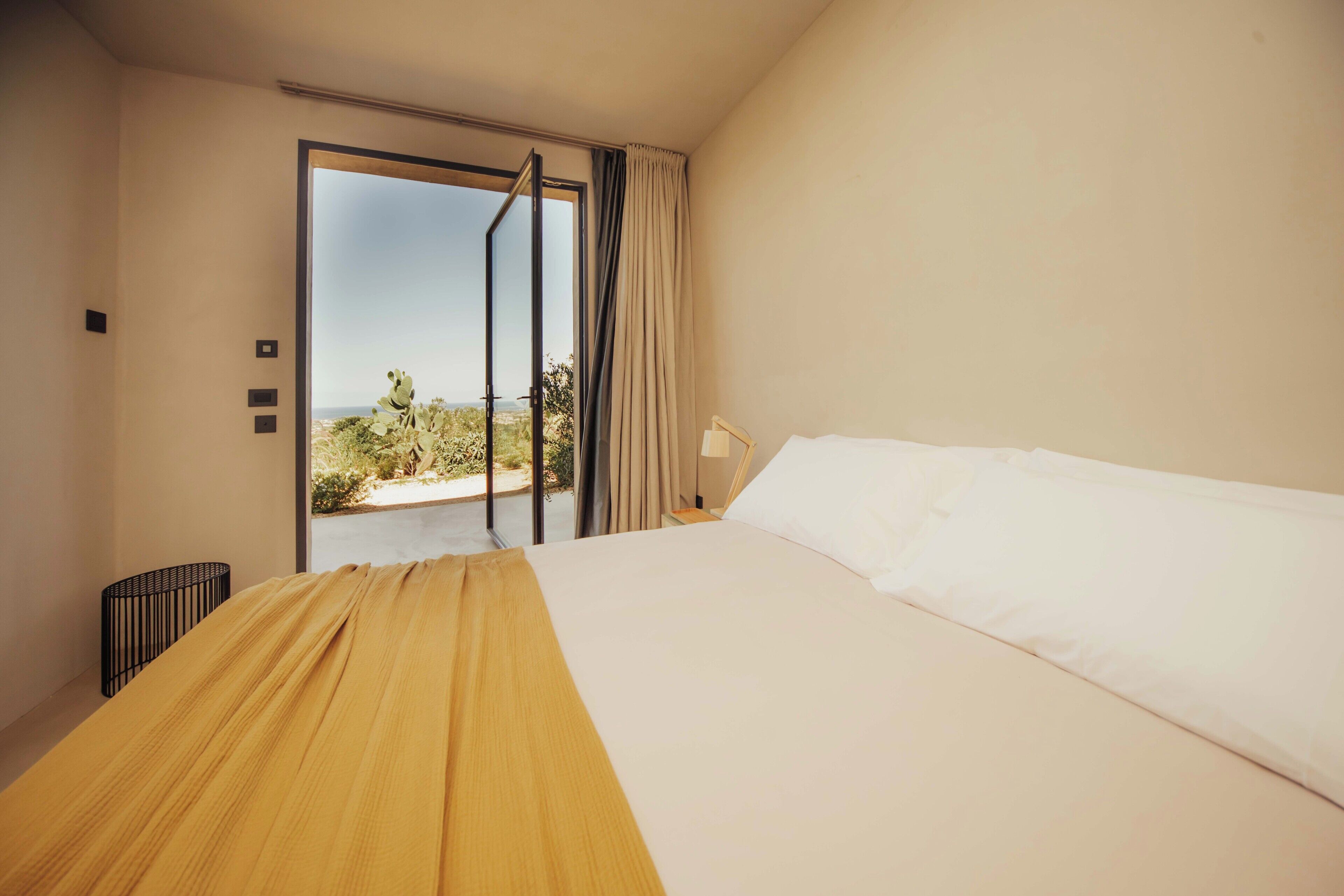 A hotel room with a bed, a view through a sliding door, and a small table with a lamp.