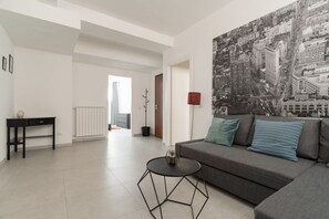 A modern living room with a sofa, a coffee table, and a cityscape painting on the wall. - A cozy 60 sqm apartment that sleeps up to 4 people, located on the semi-basement level of a building (accessible via stairs).The neighborhood is well-connected to the city center and major attractions by public transport; the Tolstoj stop on the M4 met (Milan)
