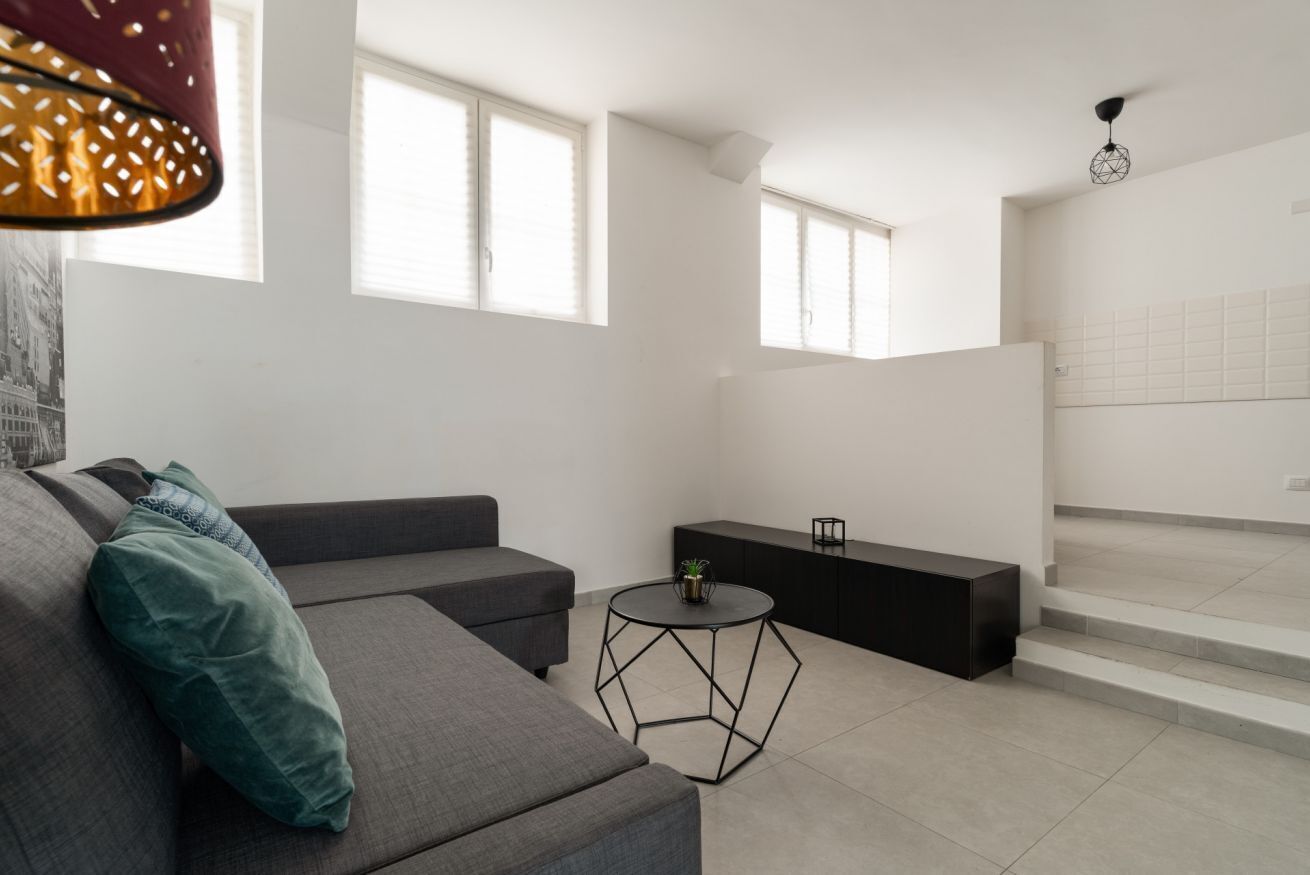 Ein modernes Wohnzimmer mit einem grauen Sofa, einem kleinen runden Tisch und einer Treppe, die zu einer oberen Ebene führt.