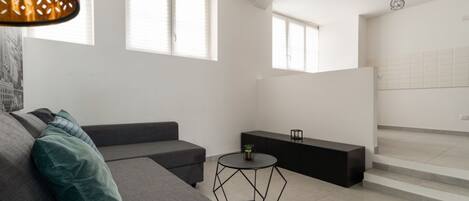 A modern living room with a grey sofa, a small round table, and a staircase leading to an upper level.