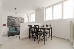 Ein Essbereich mit Tisch und Stühlen, einer Couch mit Kissen, einer Stehlampe und einem Stadtbild an der Wand.