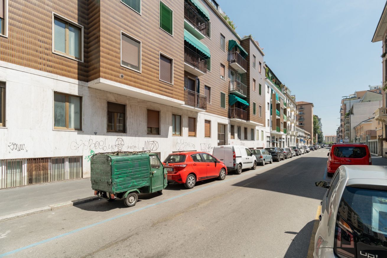 Eine Reihe moderner mehrstöckiger Gebäude mit Balkonen, parkenden Autos und einem grünen Lastwagen auf der Straße.