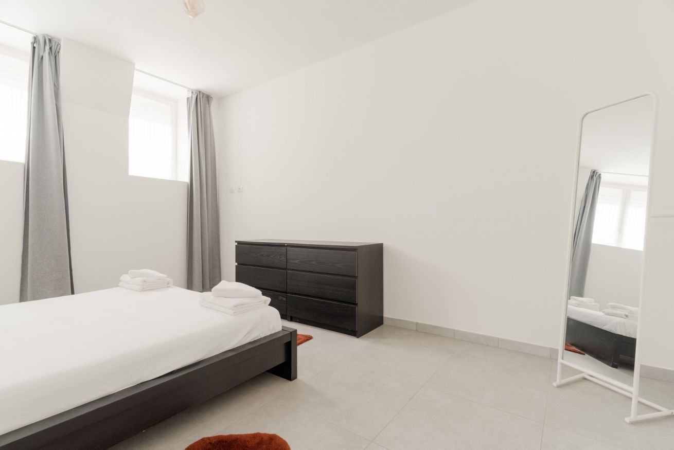 Un dormitorio moderno con una cama, un aparador y un espejo de cuerpo entero.