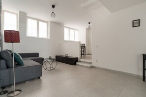 A modern living room with a grey sofa, a black coffee table, and a floor lamp. There are two windows with blinds, a staircase leading to another level, and a framed picture on the wall. - A cozy 60 sqm apartment that sleeps up to 4 people, located on the semi-basement level of a building (accessible via stairs).The neighborhood is well-connected to the city center and major attractions by public transport; the Tolstoj stop on the M4 met (Milan)