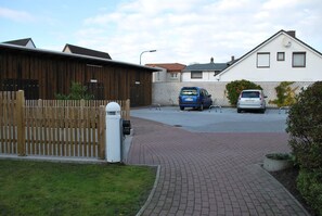 A residential street with two cars parked on the side, a wooden fence, and a paved driveway leading to a house. - Vrbo Property (Büsum)