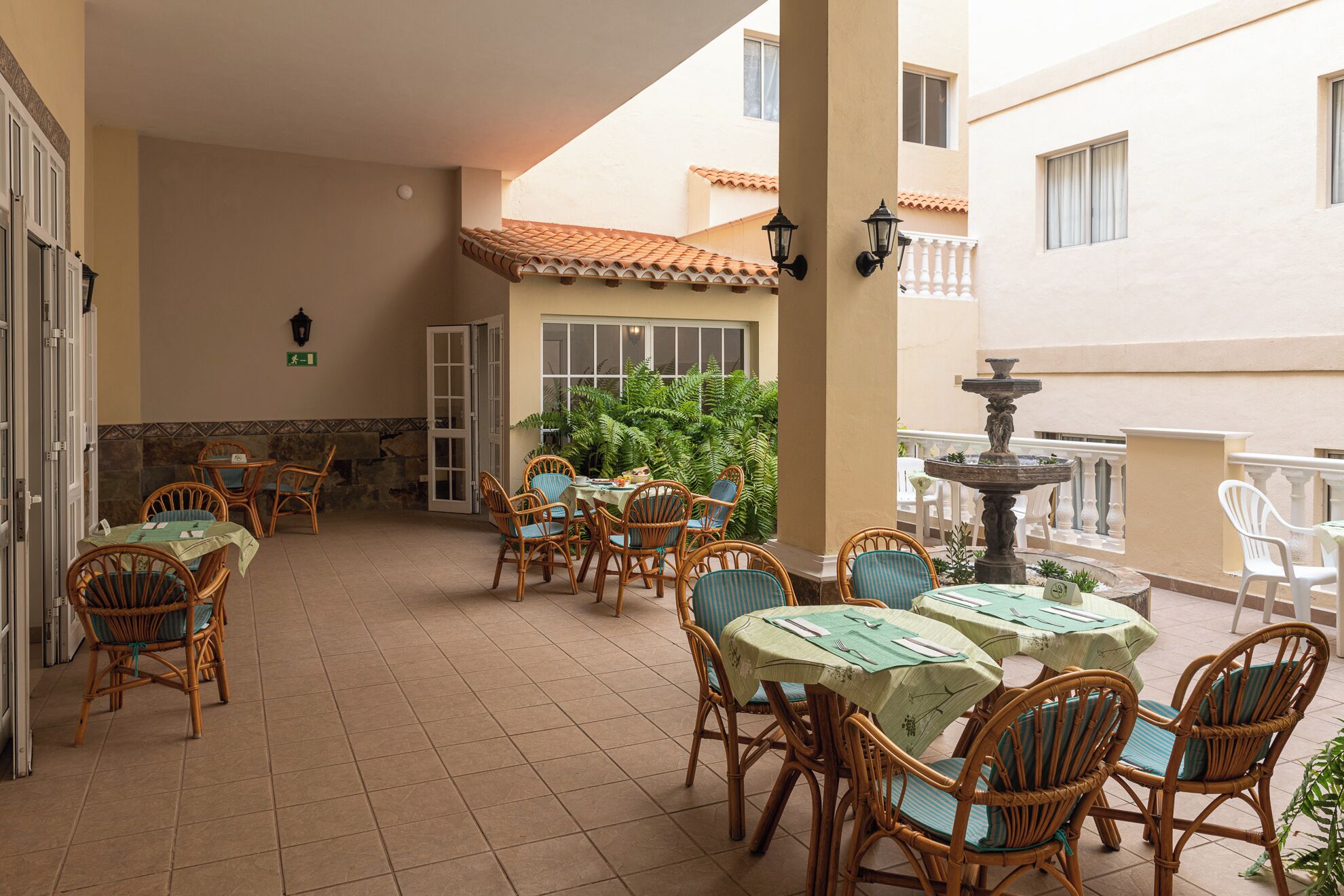Un’area patio coperta con mobili in vimini e pavimento piastrellato, che include una fontana e piante in vaso.