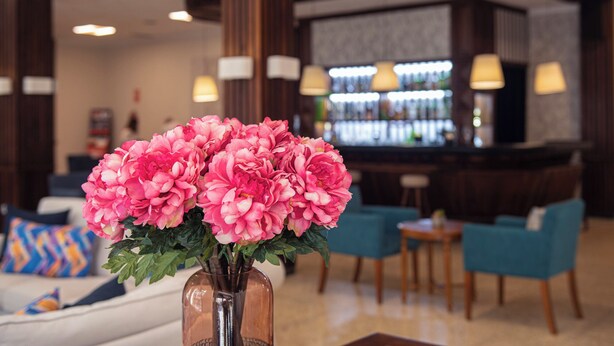 A lobby with a bar area, seating, and a vase of pink flowers. - Hotiday Tenerife Norte (Puerto de la Cruz)