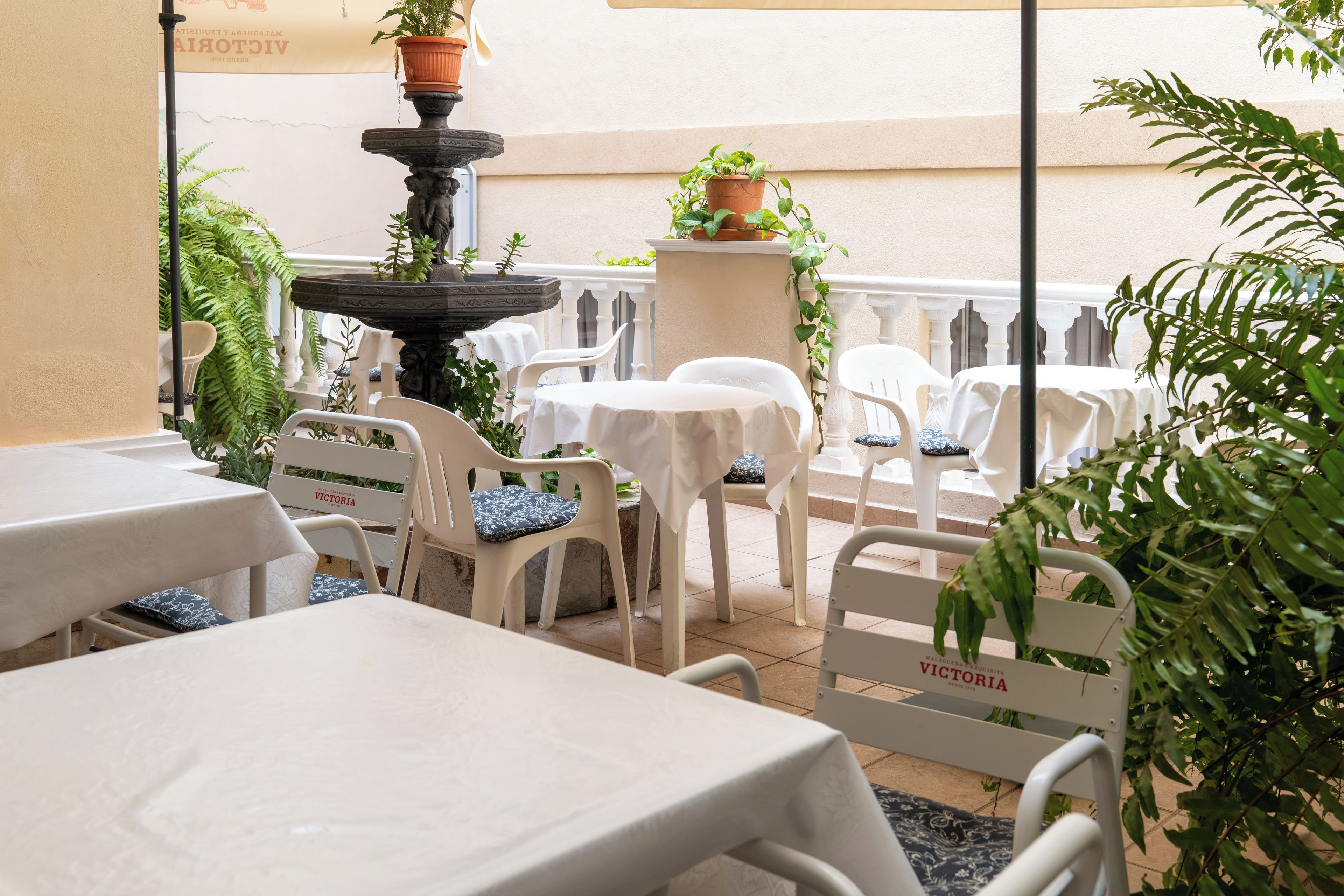 An outdoor patio area with tables and chairs, a decorative fountain, and potted plants.
